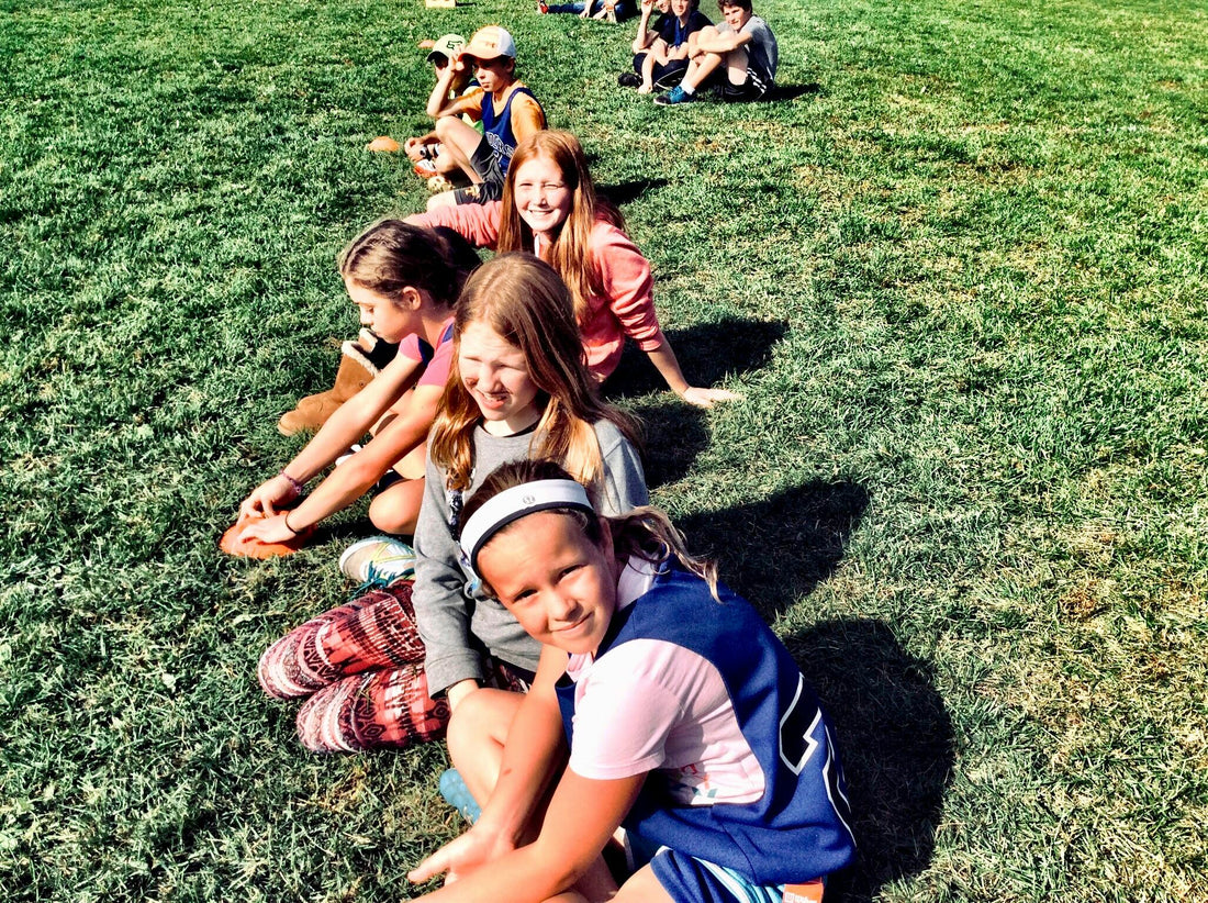 Children sitting on the grass forming a line. Looks like a warm summer day and they are about to play